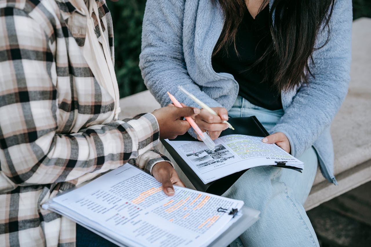 why-choose-us Crop unrecognizable multiracial female students sitting on stone bench in campus and taking notes in papers with printed texts