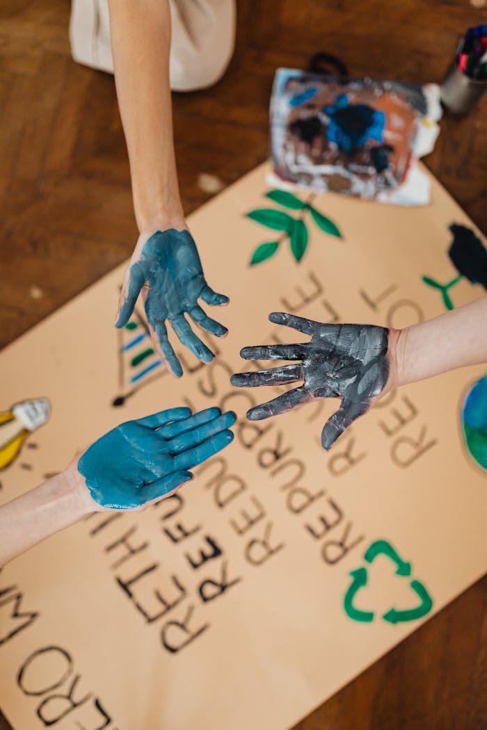 gallery-4 Hands covered in blue paint creating art with environmental themes on paper.